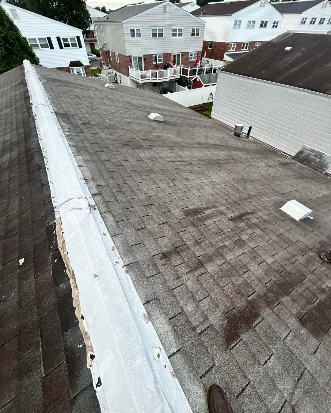 Rooftop with gray shingles overlooking neighboring houses on a residential street.