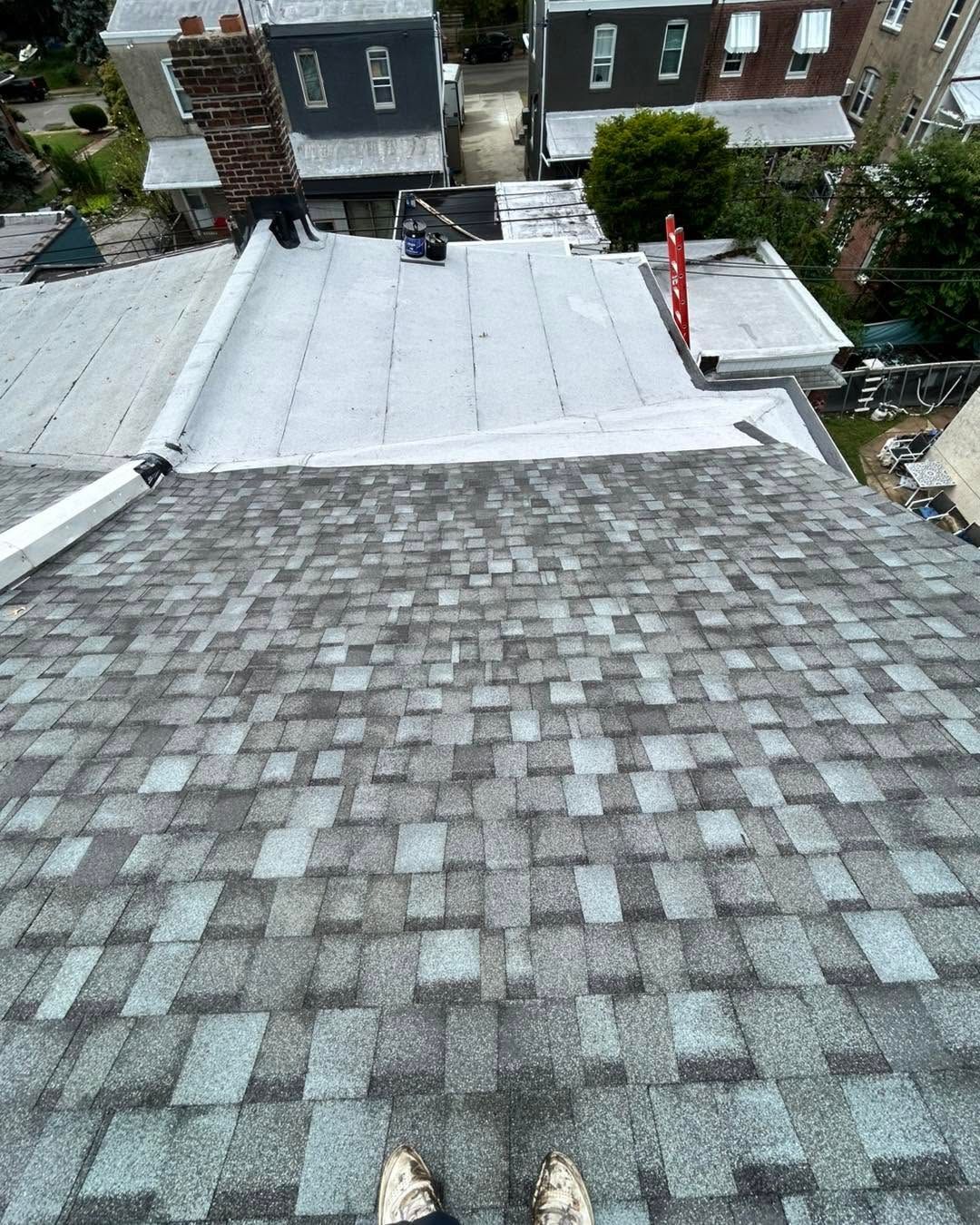 View from a shingled rooftop toward neighboring homes, with a white roof section and red ladder near the right edge