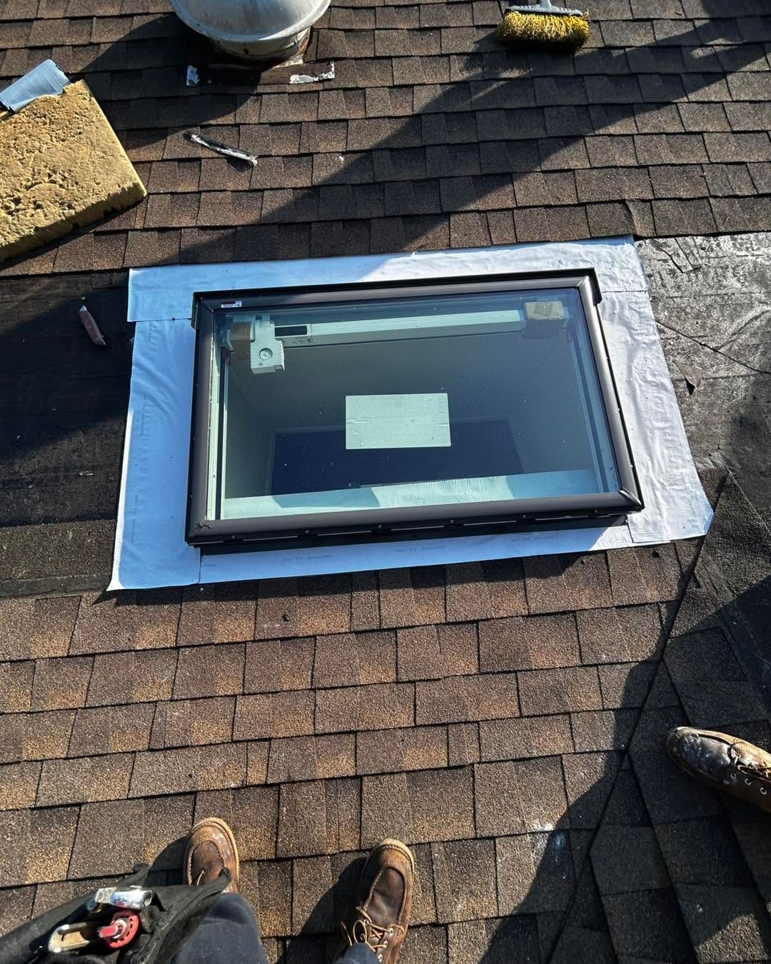 Skylight window on a shingled roof with blue protective tape around the frame