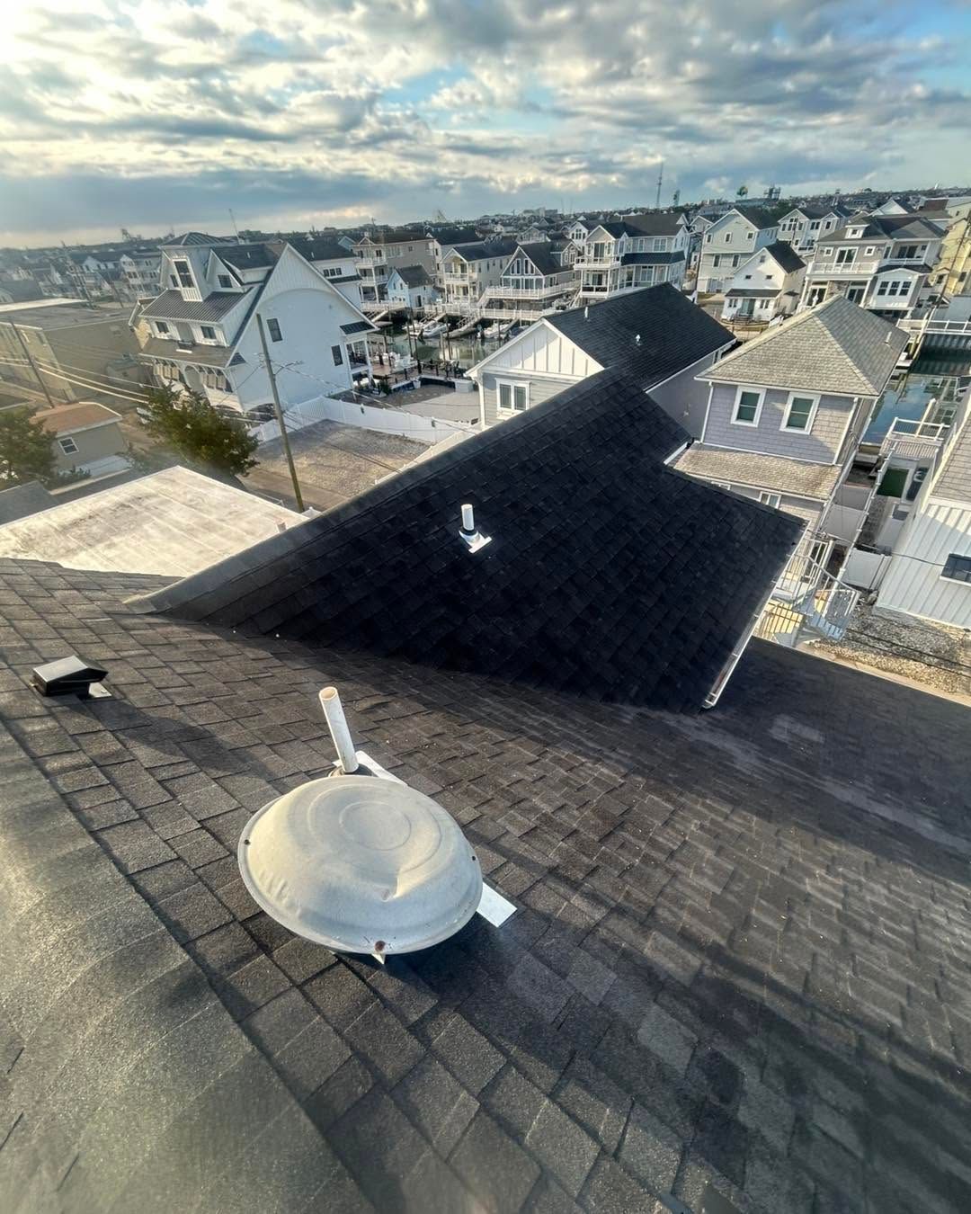 Rooftop with a white vent in the foreground, overlooking suburban houses under a cloudy sky.