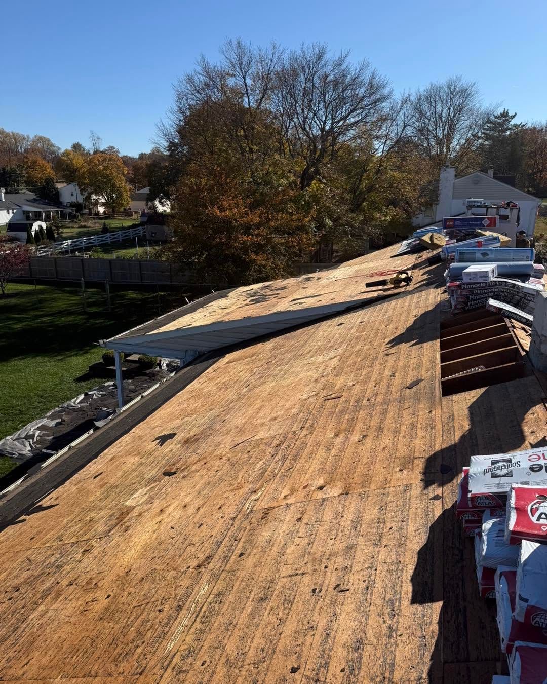 Roof under construction with plywood sheathing, shingles, and tools on a sunny day