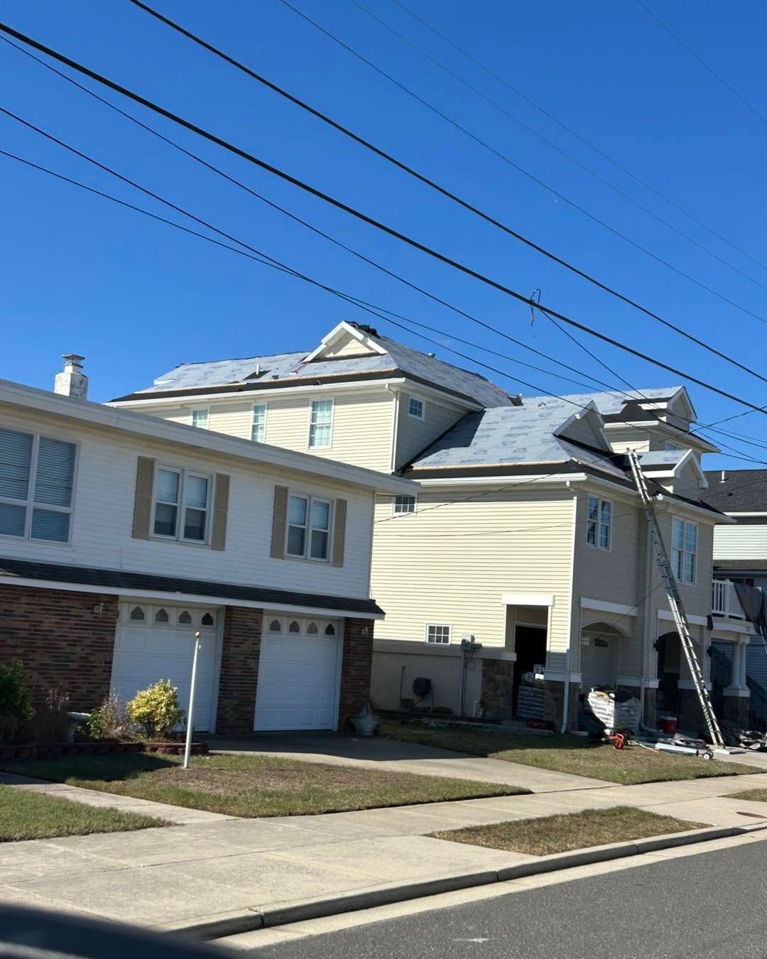 Residential houses with beige siding, a garage, and snow on the roof under a clear blue sky.