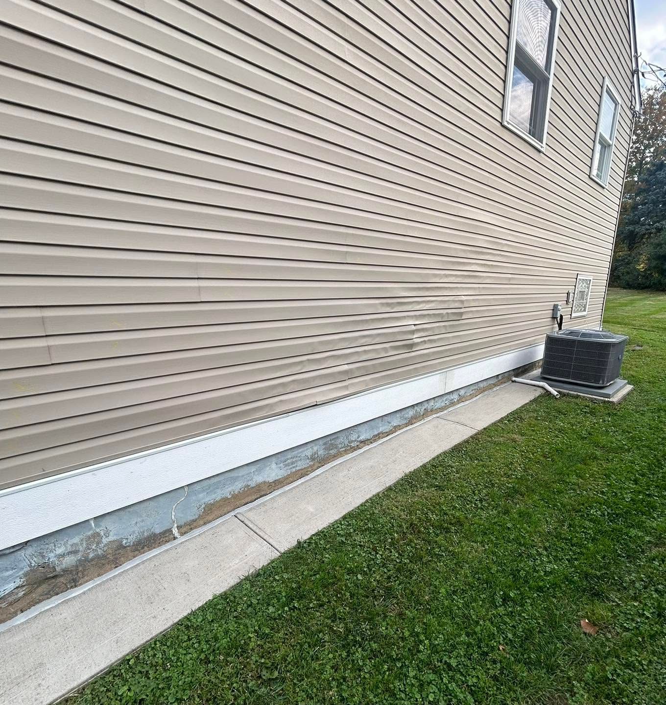Side of tan house with white foundation trim, concrete walkway, and an outdoor AC unit on the grass.
