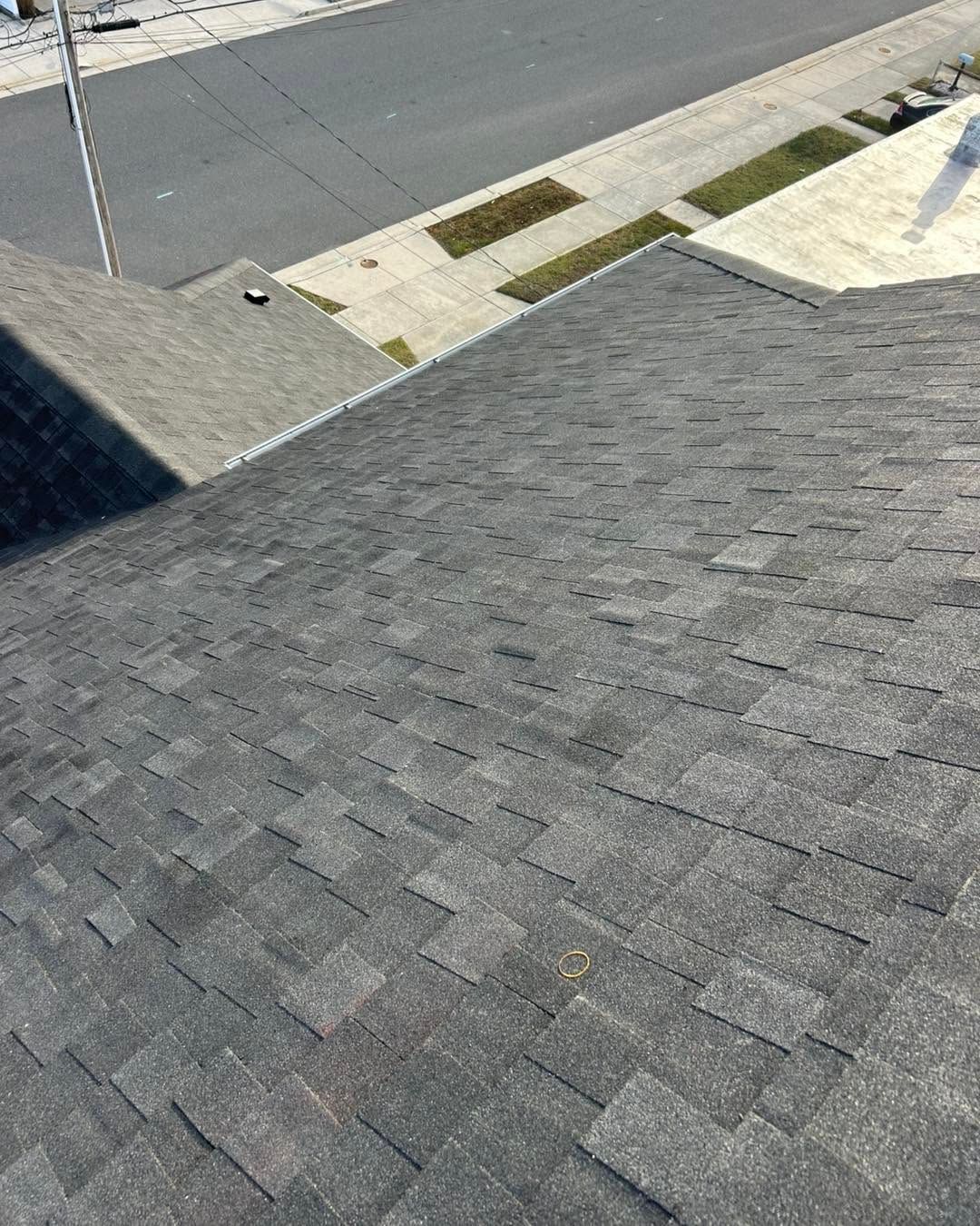 Dark gray shingled roof with a street and sidewalk visible below in bright daylight