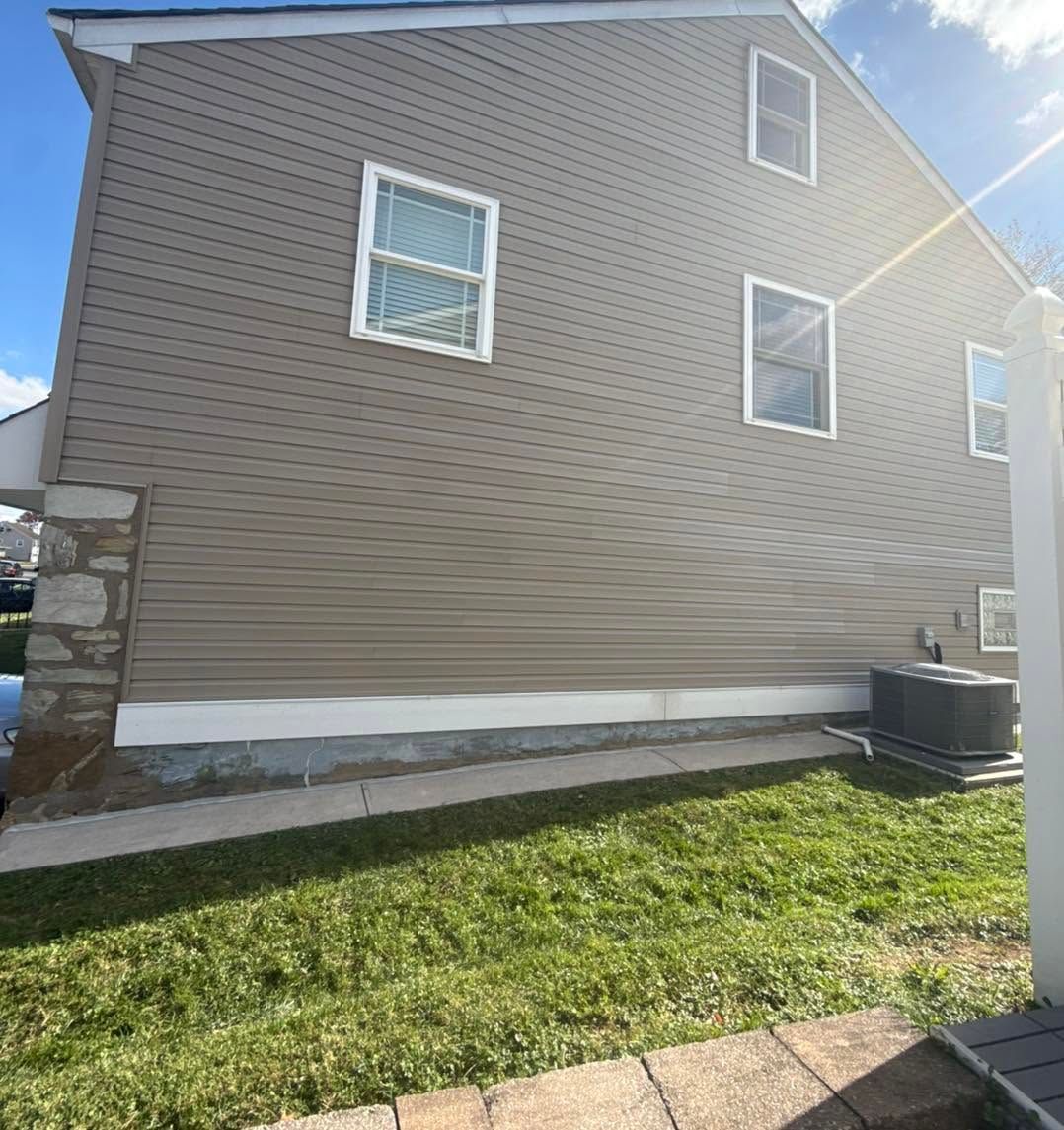 Side view of a brown house with white trim, small windows, and a grassy yard in sunlight.