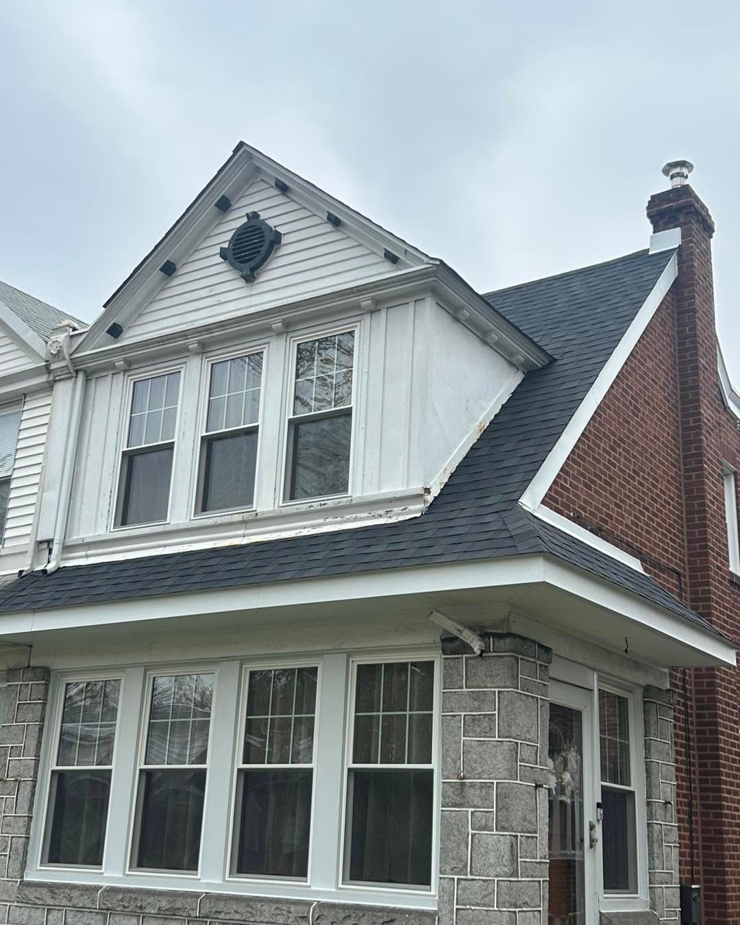 Two-story house with gray shingle roof, white siding, stone facade, and red brick side wall