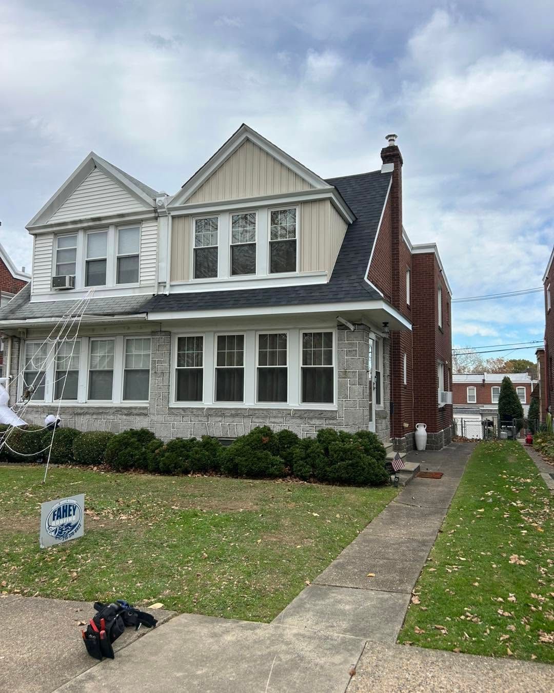 Two-story gray house with white trim, front lawn, and a walkway under a cloudy sky.
