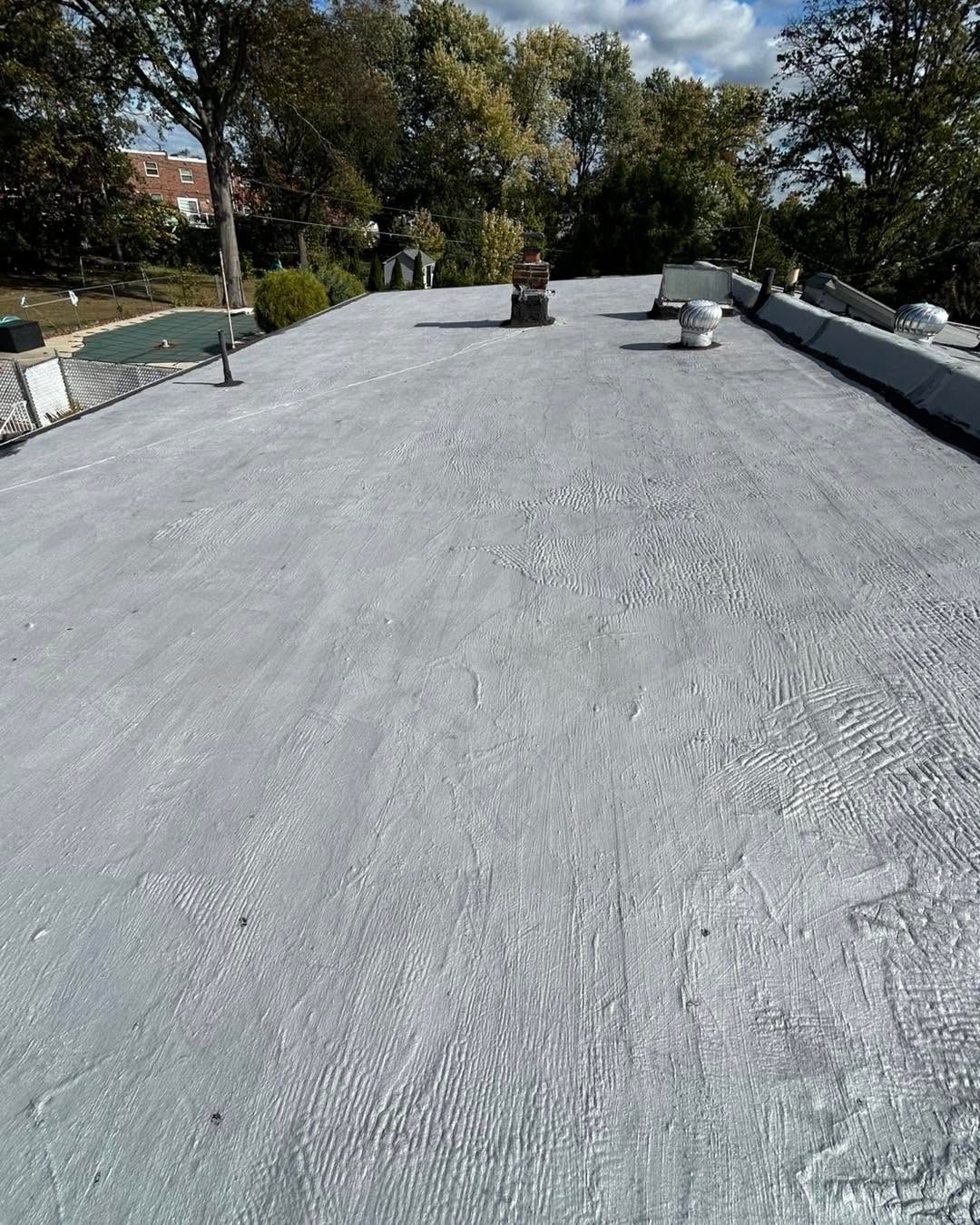 Flat gray rooftop with vents and surrounding trees on a sunny day