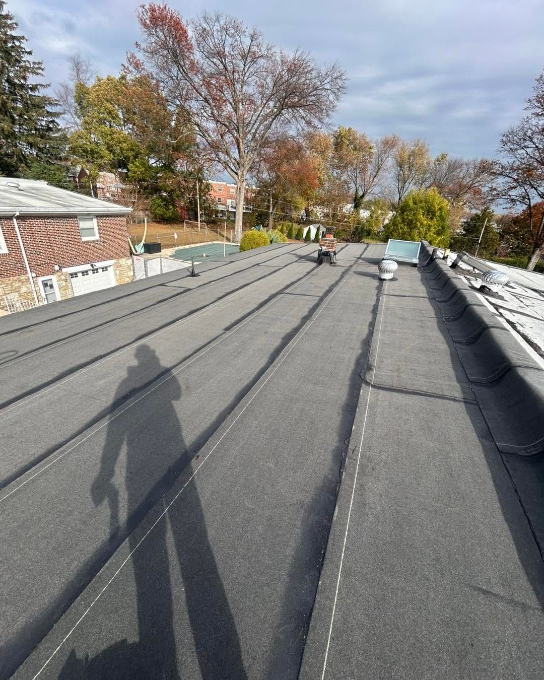 Flat rooftop with dark membrane, vents, and autumn trees under a cloudy sky