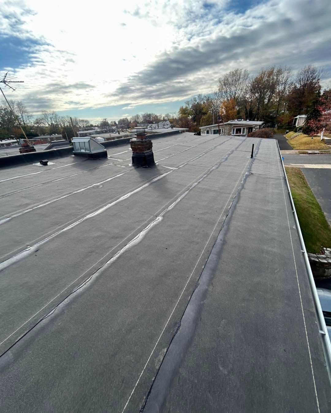 Flat rooftop with dark membrane roofing, vents, and a cloudy sky in the background.
