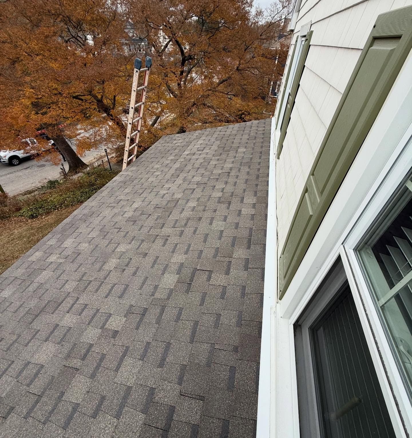 Gray shingled roof beside a house window, overlooking autumn trees and a street below