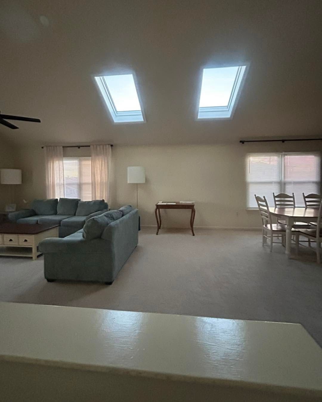 Spacious living room with skylights, gray sectional sofa, dining table, and beige carpet.