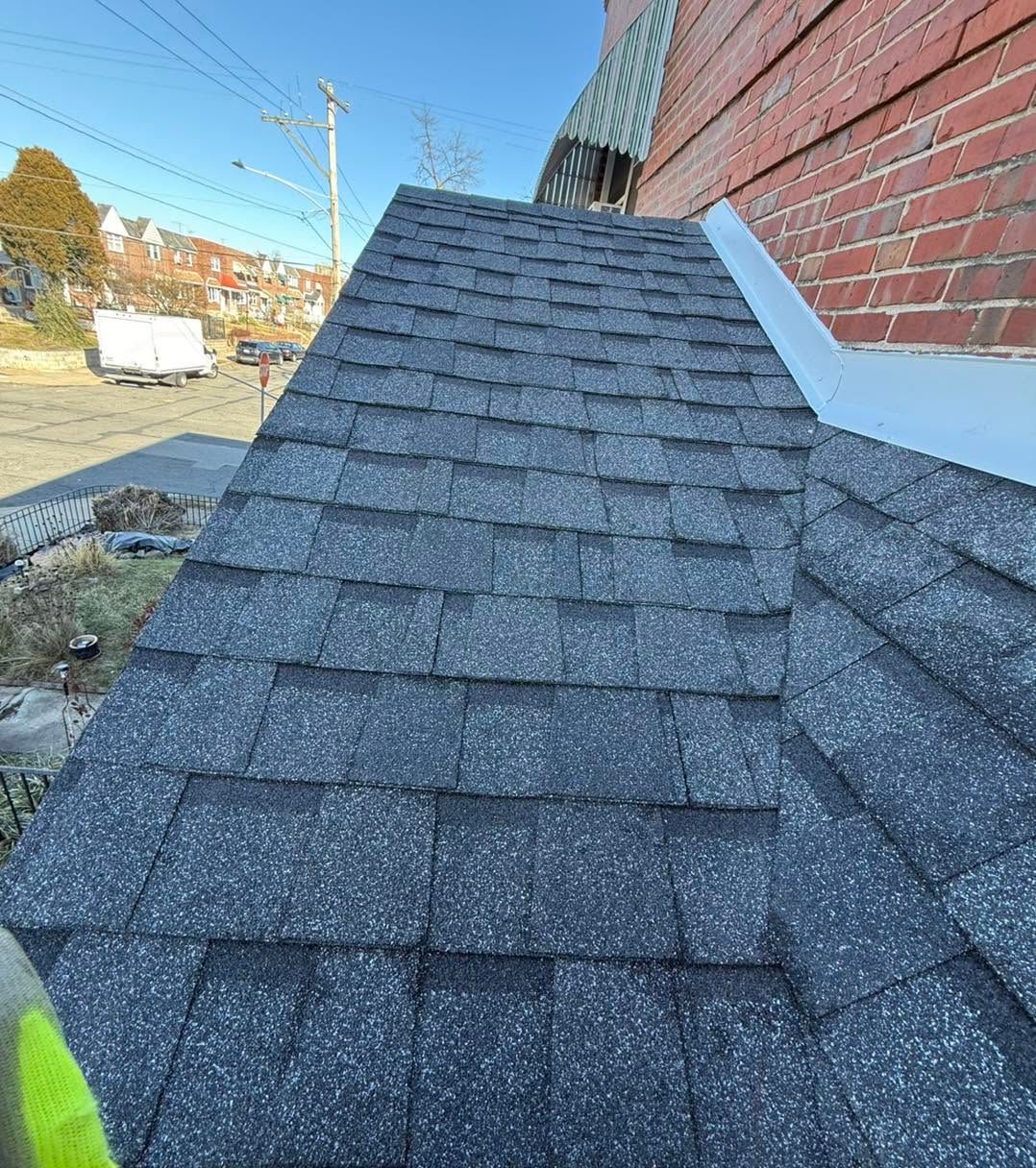 Gray shingled roof section beside a red brick wall, seen from above.