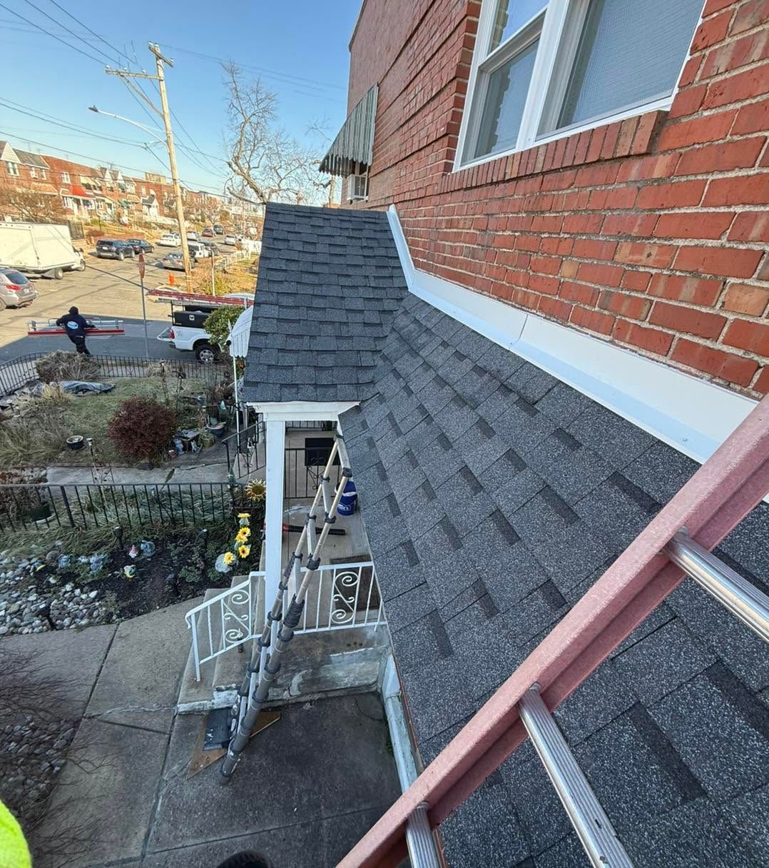 Brick house exterior with steep gray shingled roof, white trim, and a narrow stairway below