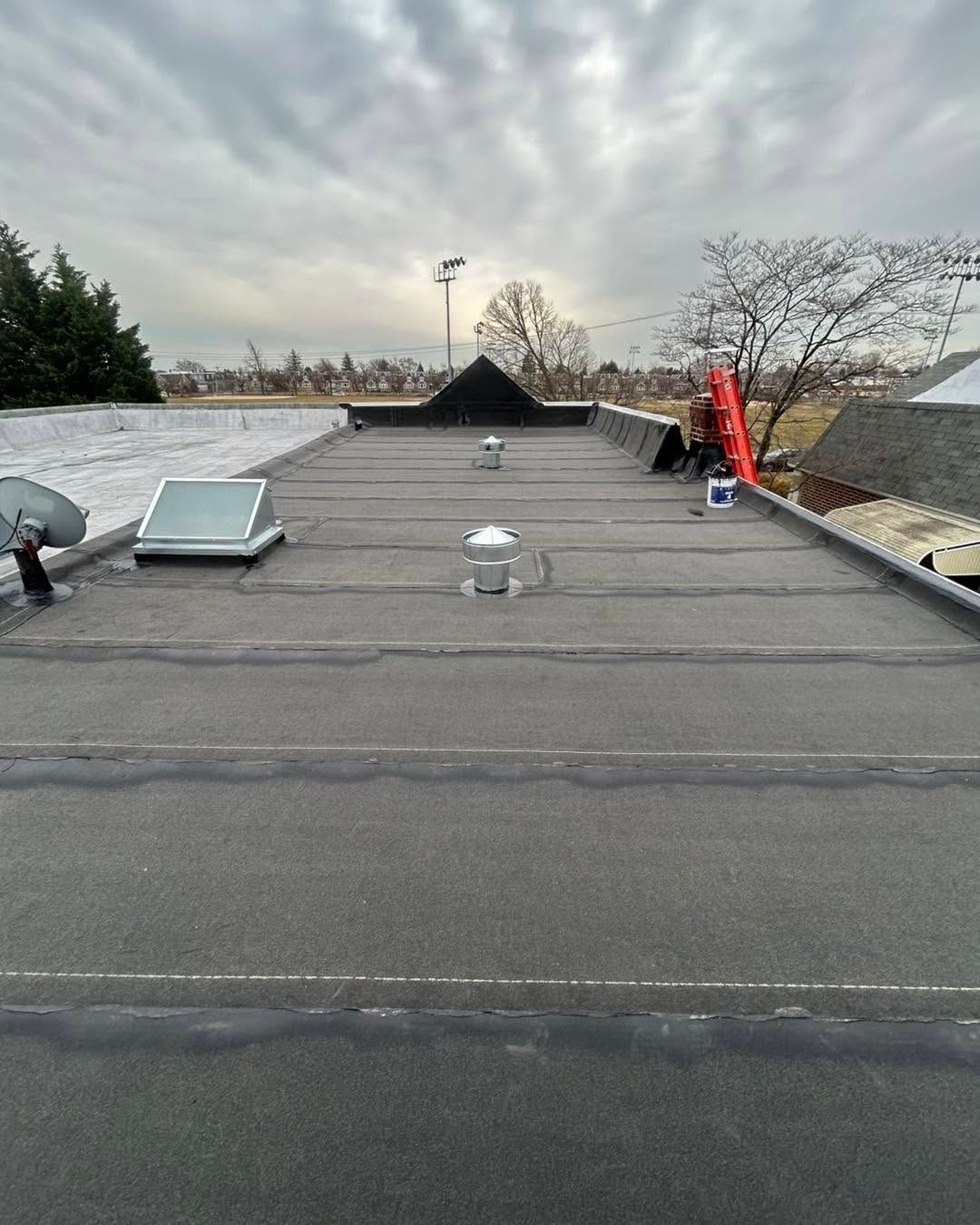 Flat rooftop with vents, skylight, and a red safety flag under an overcast sky.