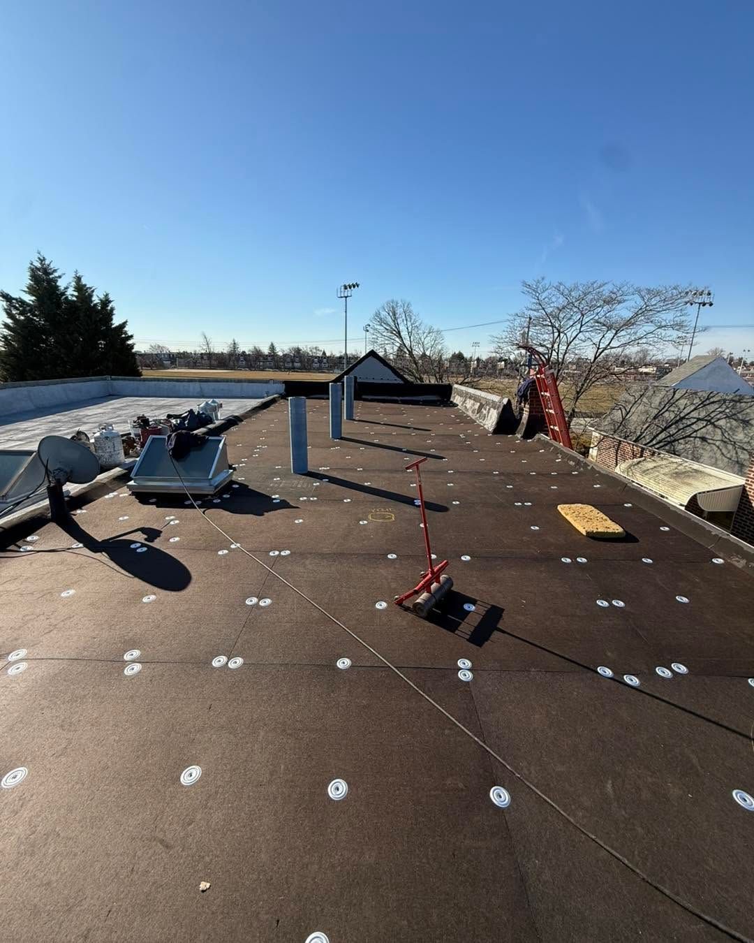 Rooftop with dark roofing, scattered equipment, and blue sky over distant landscape