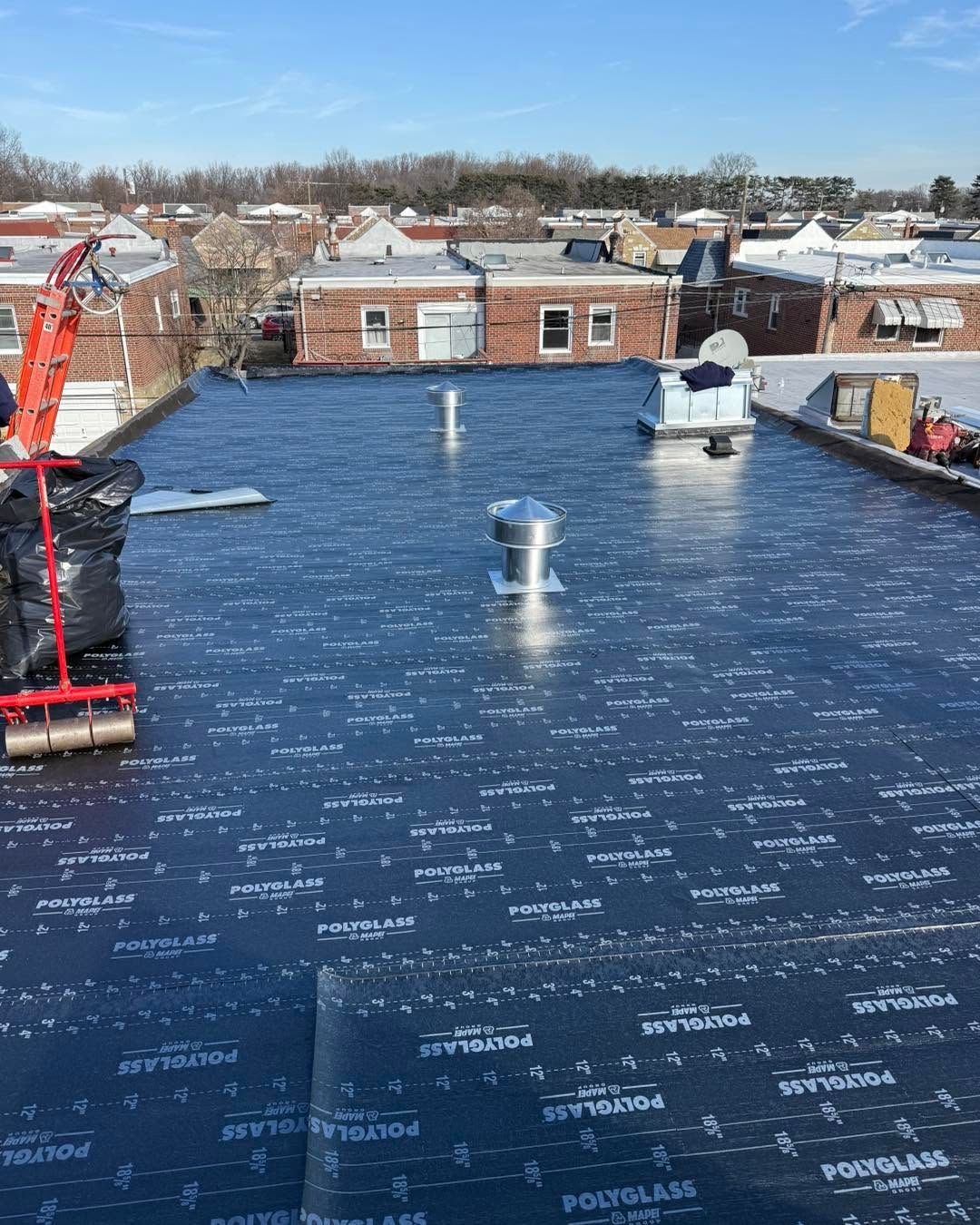 Flat black roofing membrane on a low-rise building, with vents and snowy rooftops in the background.