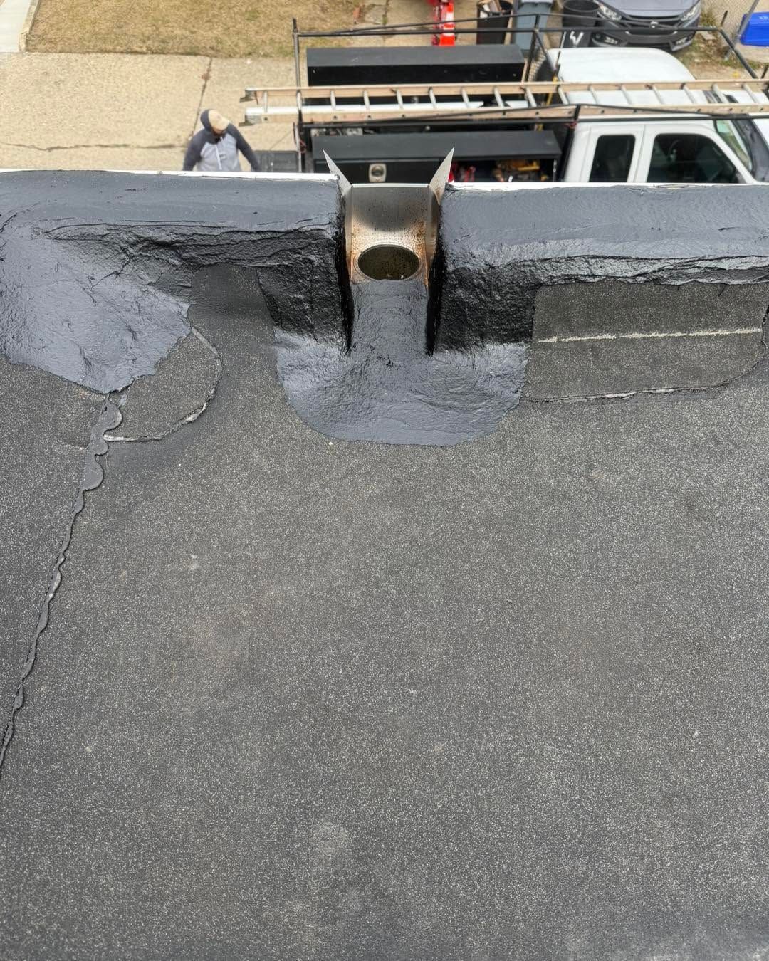 Rooftop with black waterproofing and a central pipe opening near the parapet edge.