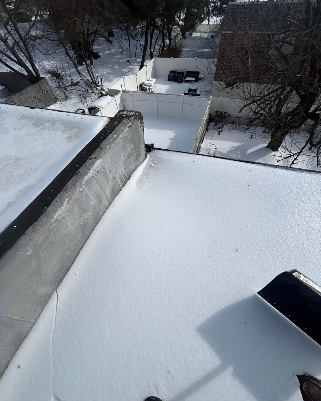 Snow-covered rooftop overlooking a snowy yard with bare trees and a small driveway.