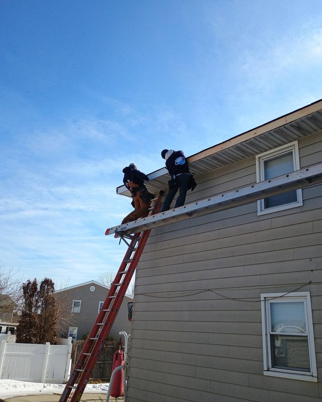 Firefighters on a ladder rescuing someone from a second-story roof on a beige house