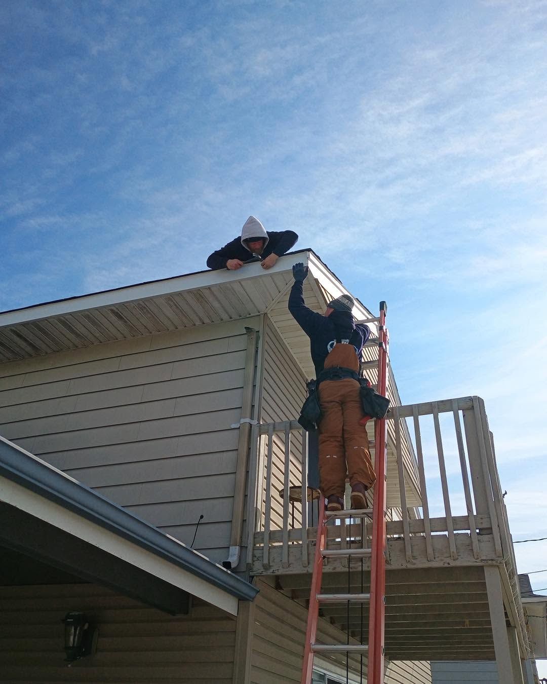 Worker on a red ladder repairing the roof edge of a house under a blue sky.