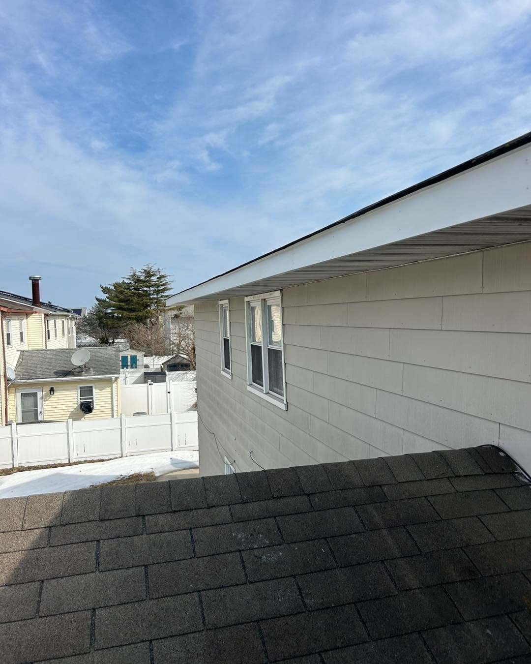 Snowy residential rooftop with gray siding and windows under a blue sky