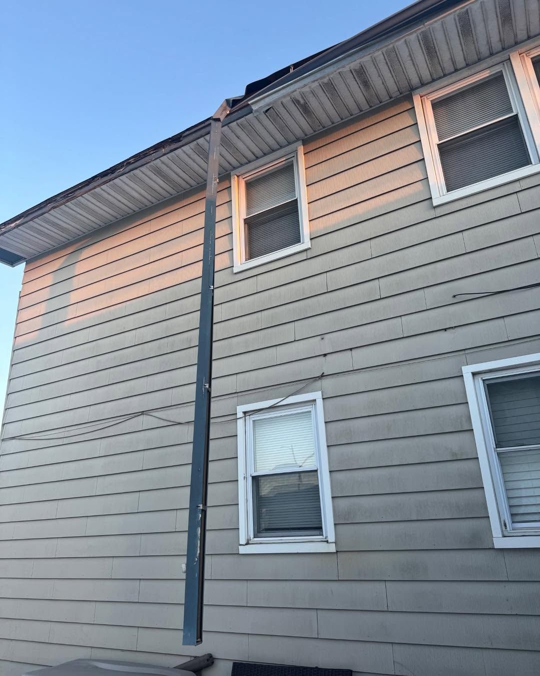 Side of a gray-beige house with white-trimmed windows and dark roof gutters