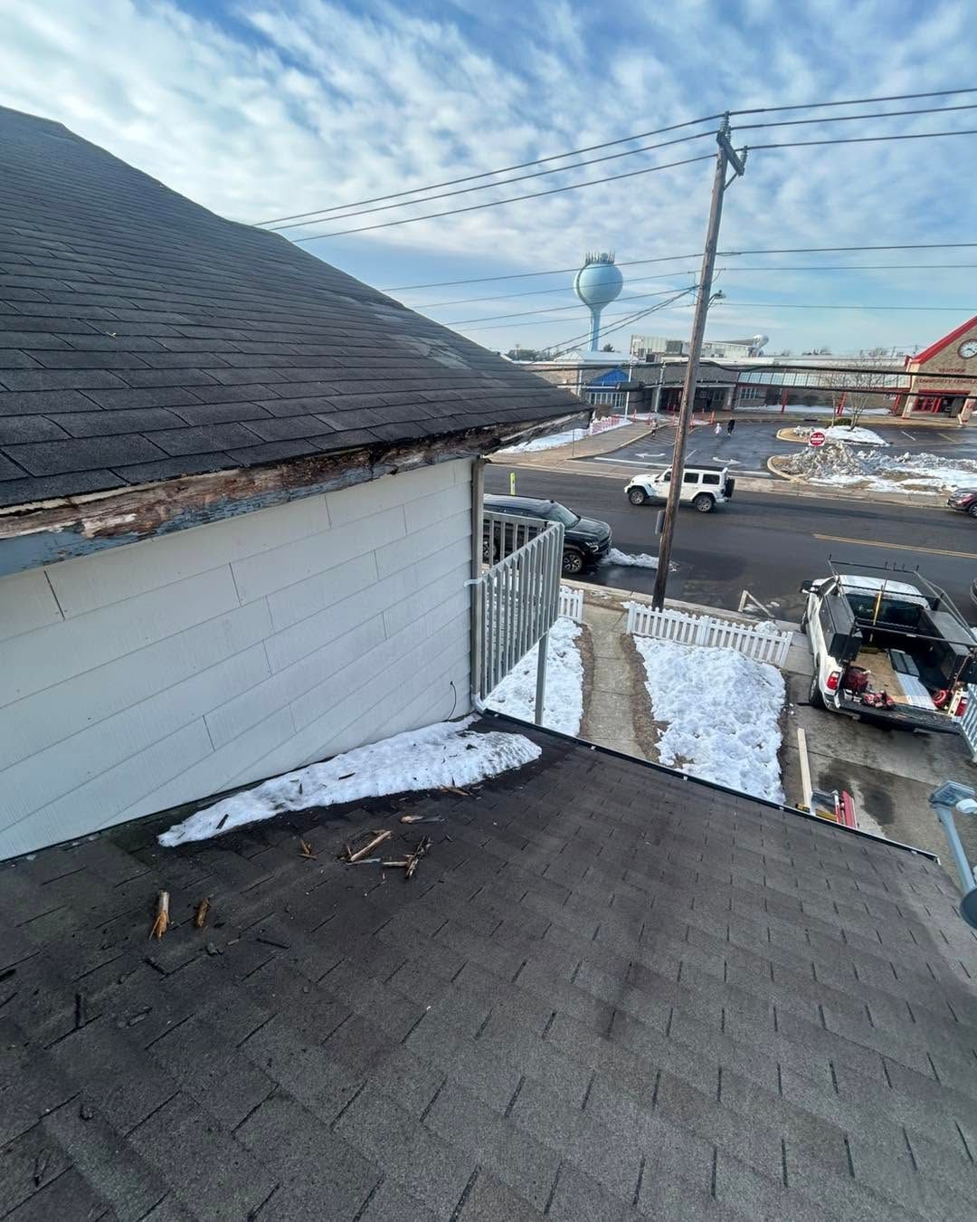 Snowy rooftop and white house siding overlooking a street with parked cars and utility lines.