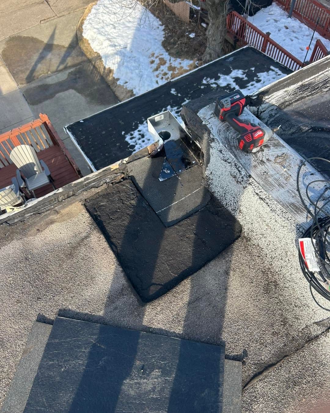 Roof view of a snowy yard with a small red excavator and rooftop shadows