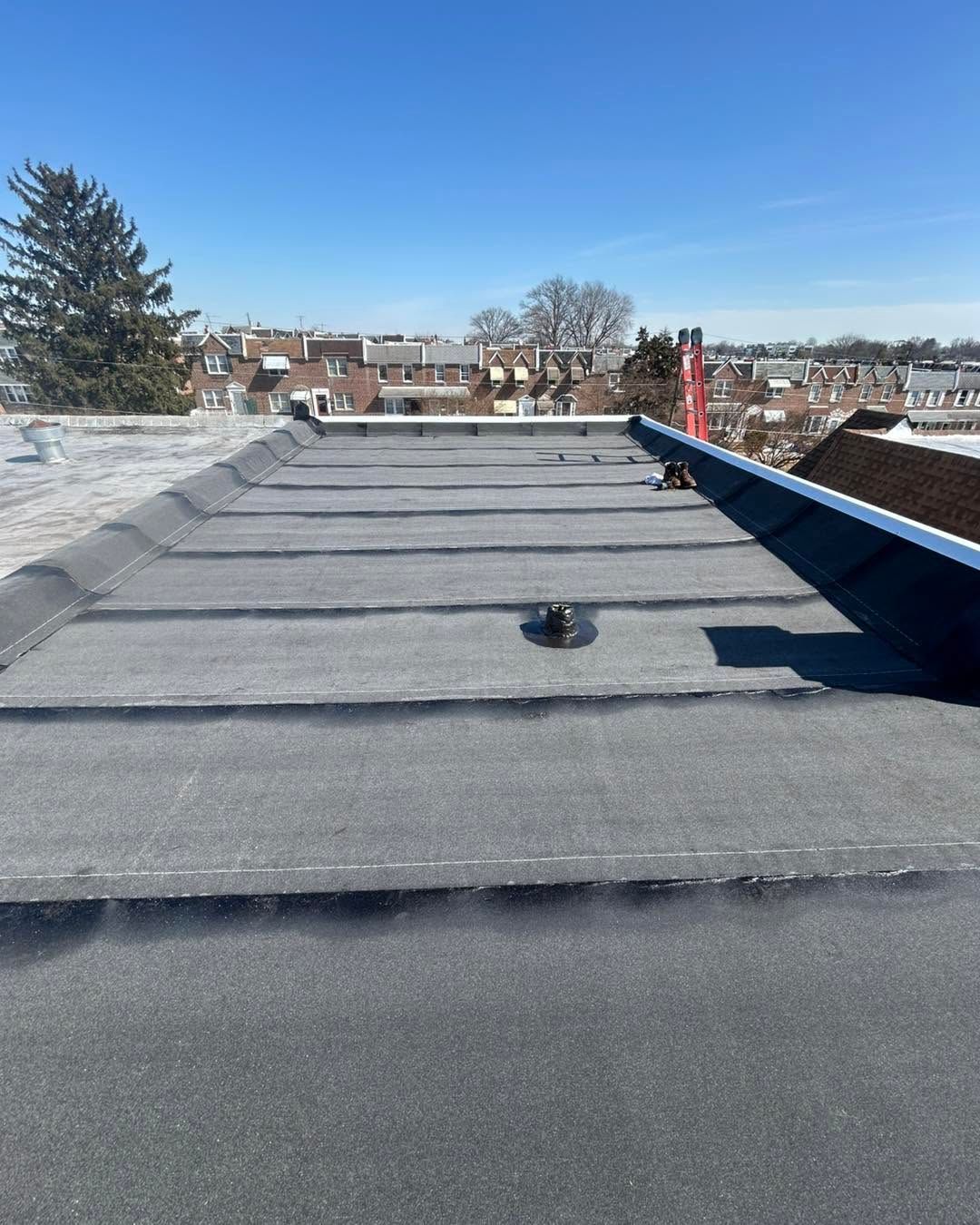 Rooftop covered in gray membrane with a blue-edged parapet, overlooking a neighborhood on a clear day