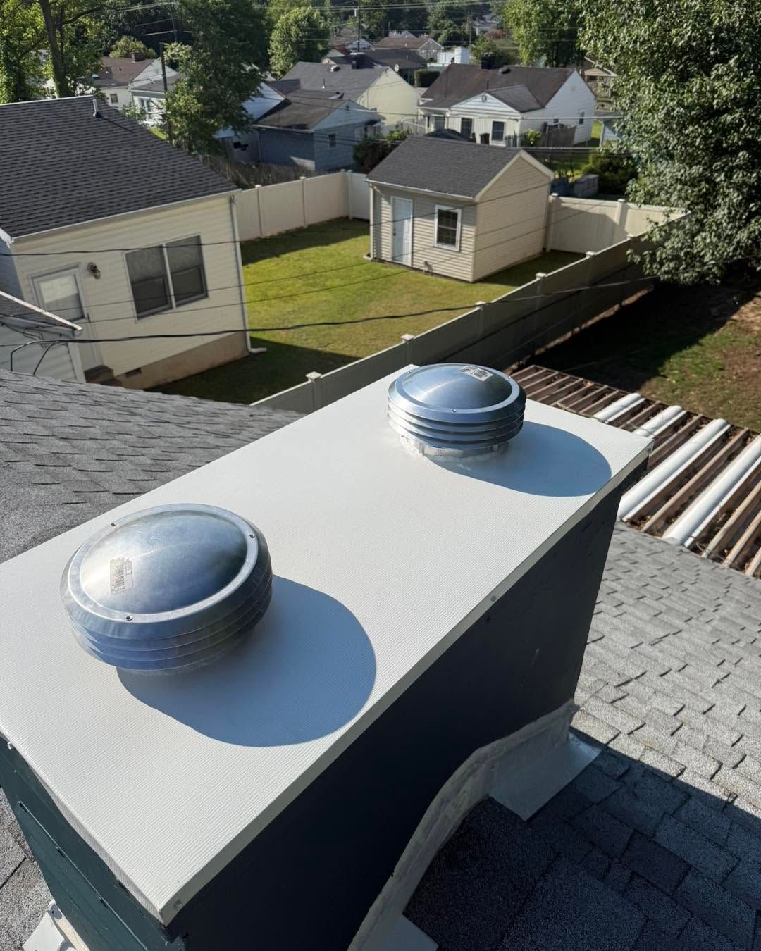 Rooftop with two silver vents overlooking a residential backyard and neighboring houses