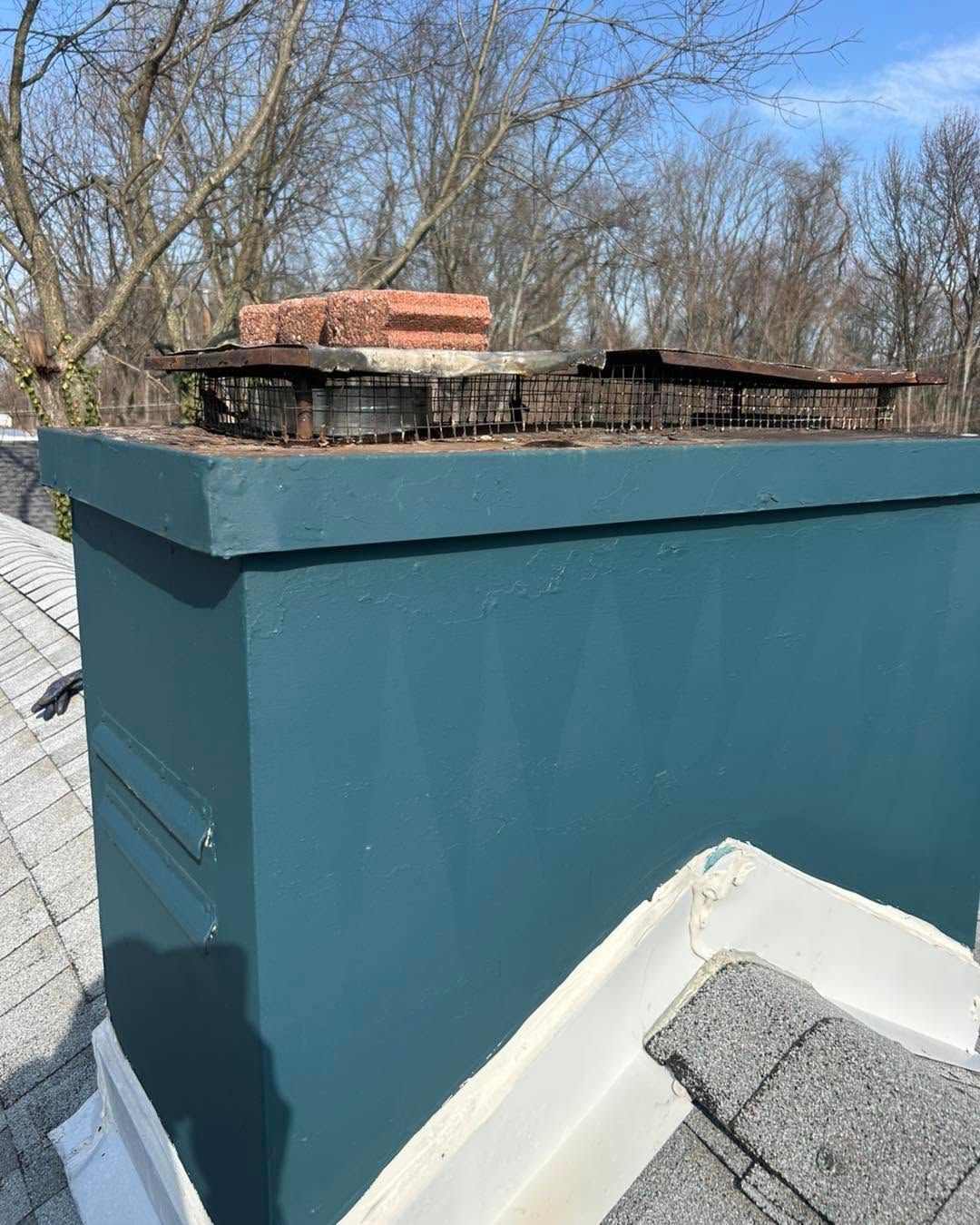 Teal rooftop utility box with metal cap and brick chimney behind it on a sunny day