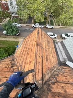Worker repairing a copper roof ridge above a street with parked cars below.
