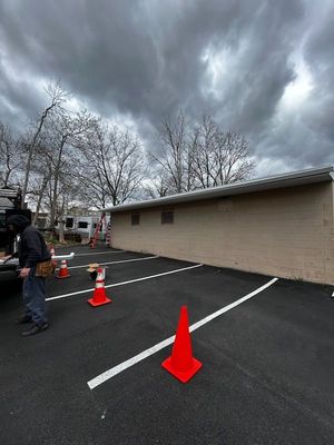 Orange cones line an empty parking lot beside a beige building under a cloudy sky.
