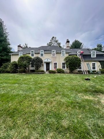 Large gray house with white trim and a broad green lawn under a cloudy sky