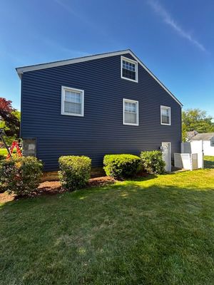 Blue house with white trim and small hedges beside a green lawn on a sunny day