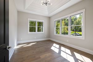 Empty bright room with white walls, wood floors, and large windows casting sunlight on the floor