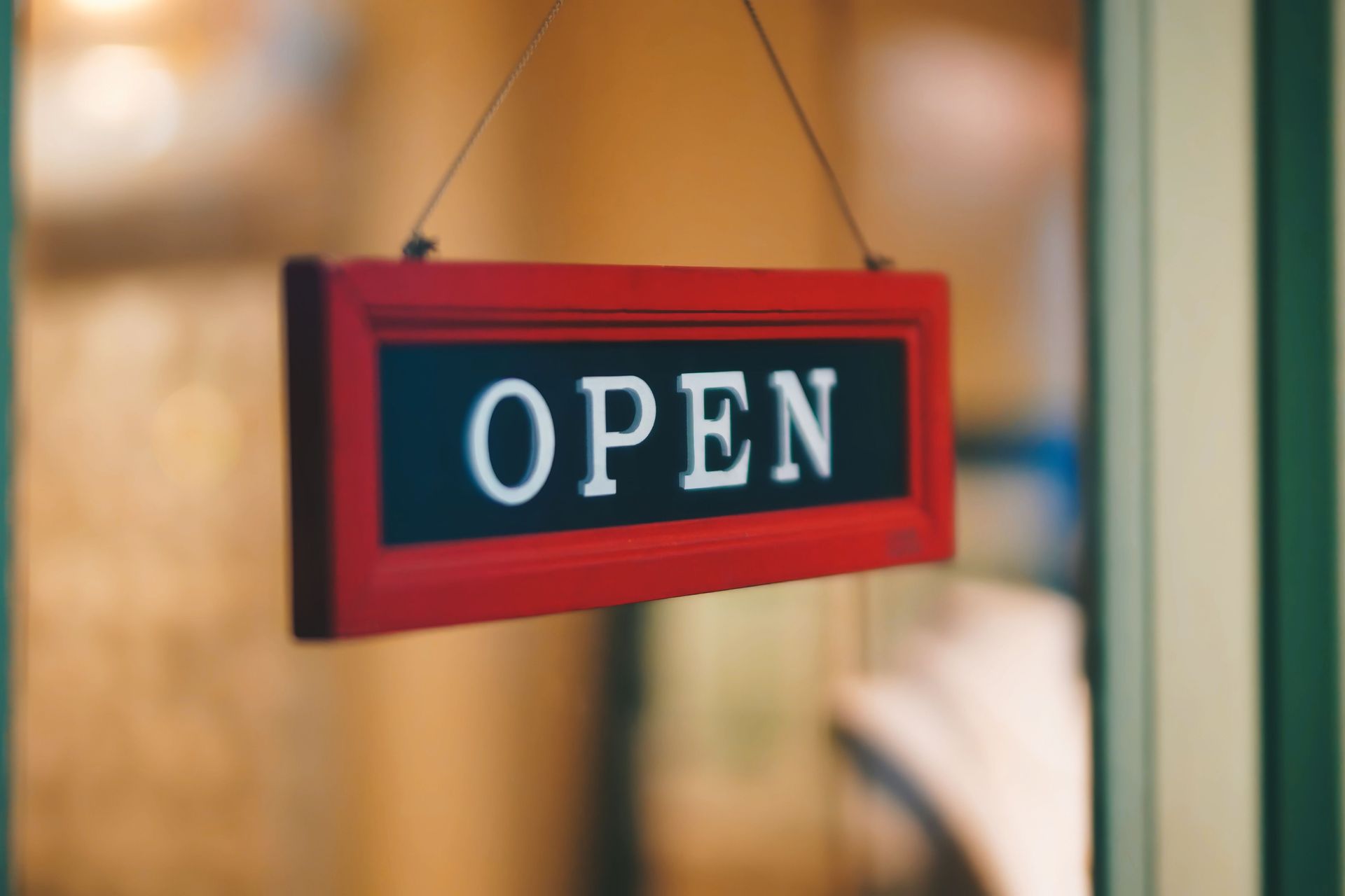 Red hanging sign reading “OPEN” on a blurred storefront background