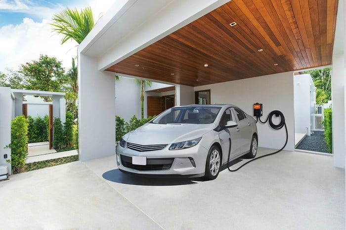 Electric car charging in a bright garage beside a wall-mounted charger