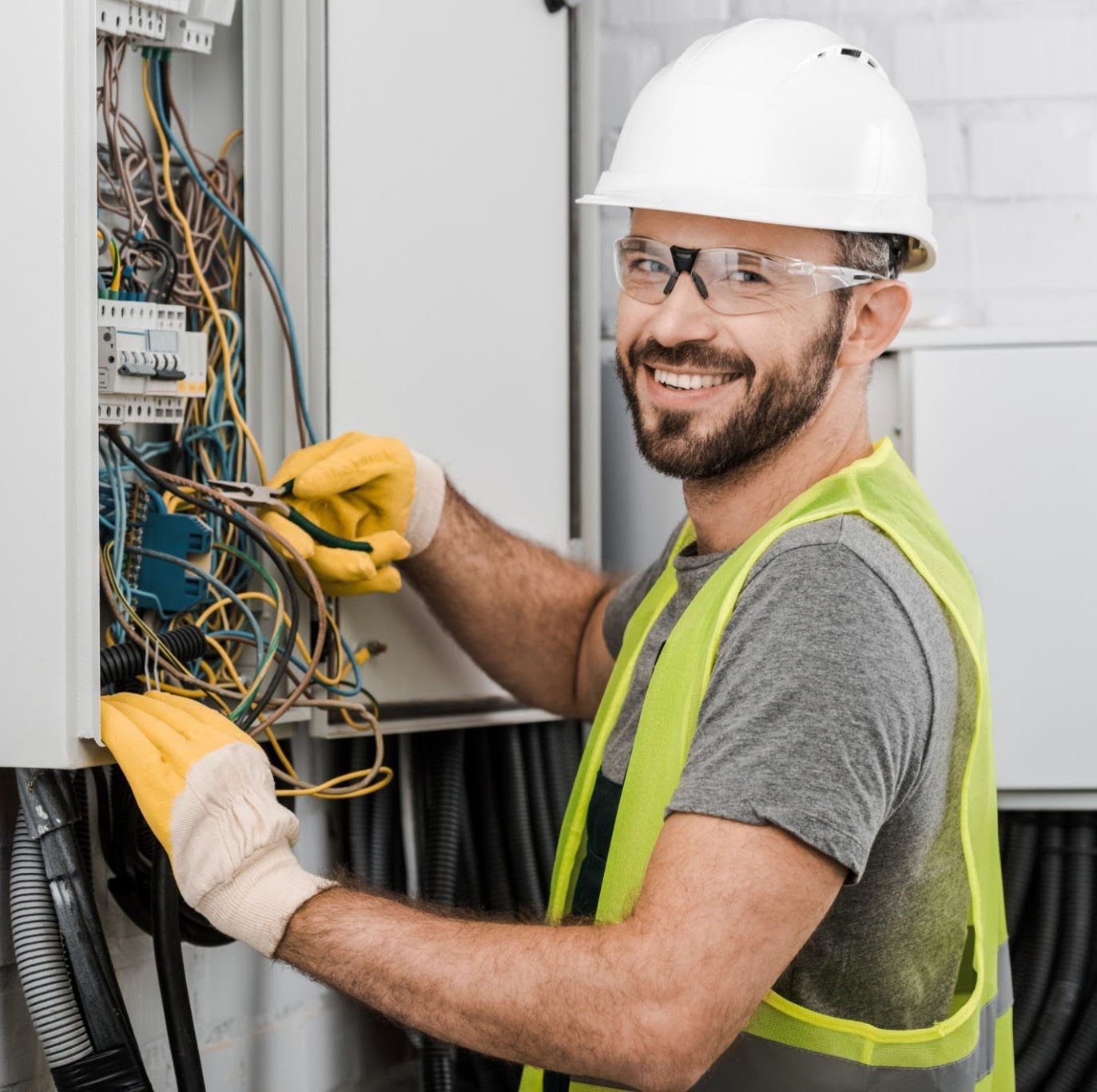 Two electricians working on an open electrical panel in a white room