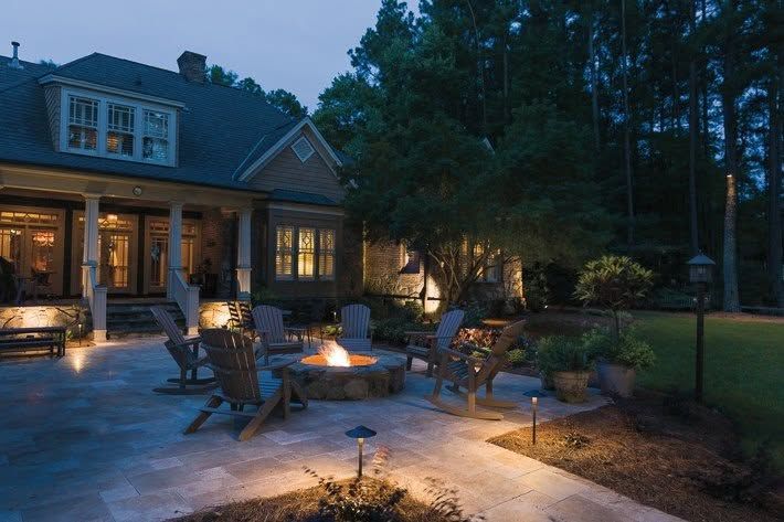 Twilight patio with fire pit, outdoor chairs, and a lit house surrounded by trees