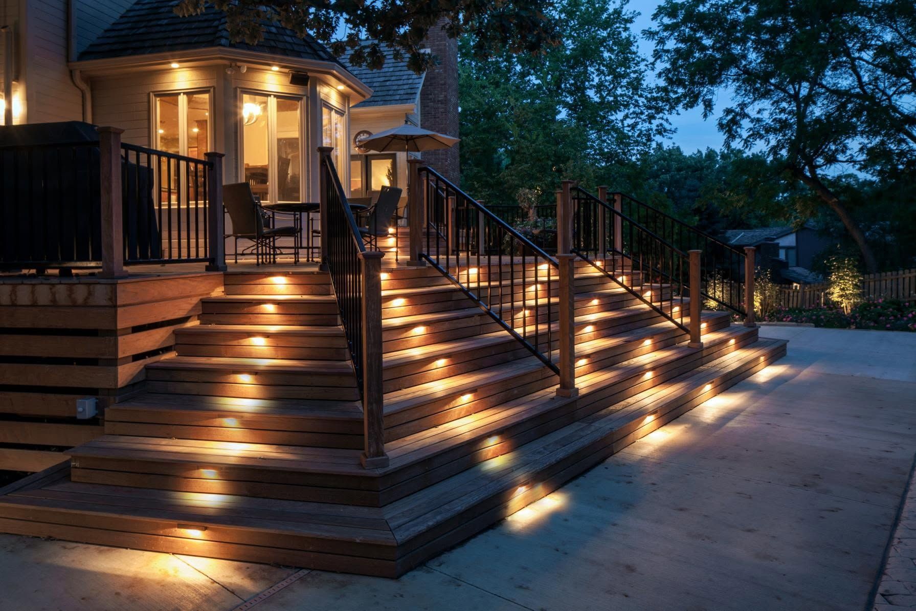 Warmly lit house porch and stairs at dusk, with glowing step lights and a quiet driveway.
