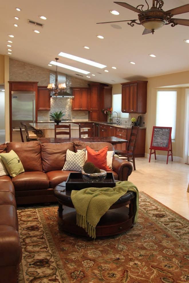 Open-plan living room with brown leather sofa, patterned rug, ceiling fan, and kitchen bar seating