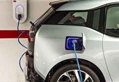 White electric car charging at a wall-mounted station in a garage, with blue charging cable connected.