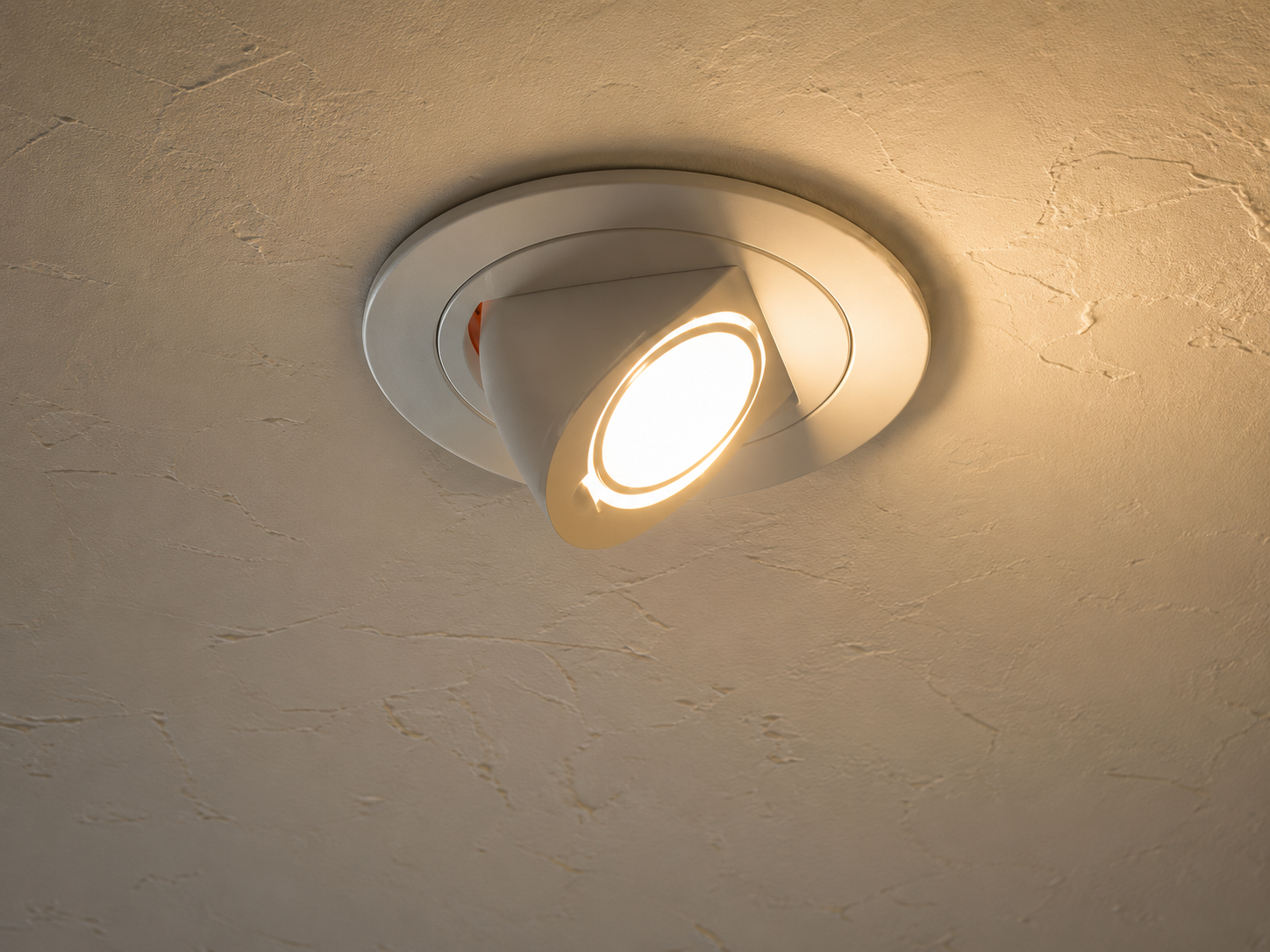 Ceiling-mounted recessed spotlight with a warm bulb on a beige textured ceiling