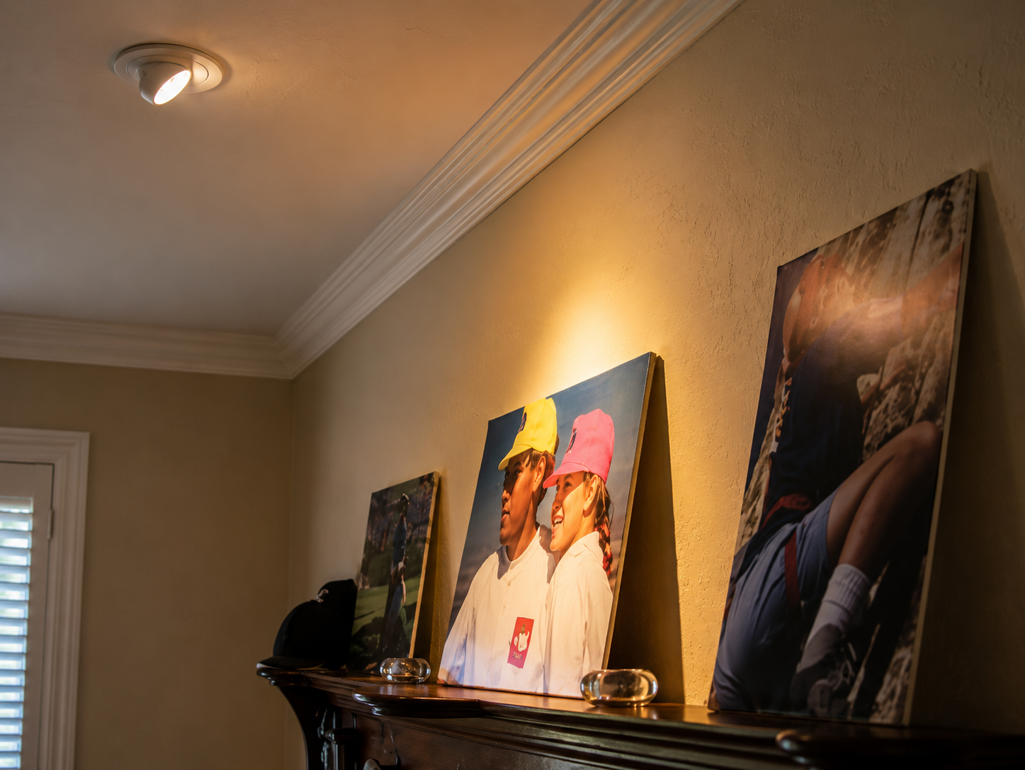 Framed wall art above a shelf in a warmly lit hallway with beige walls and crown molding