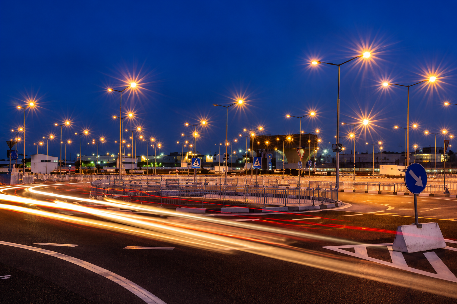 Nighttime street scene with light trails, streetlights, and a blue road sign near a roundabout