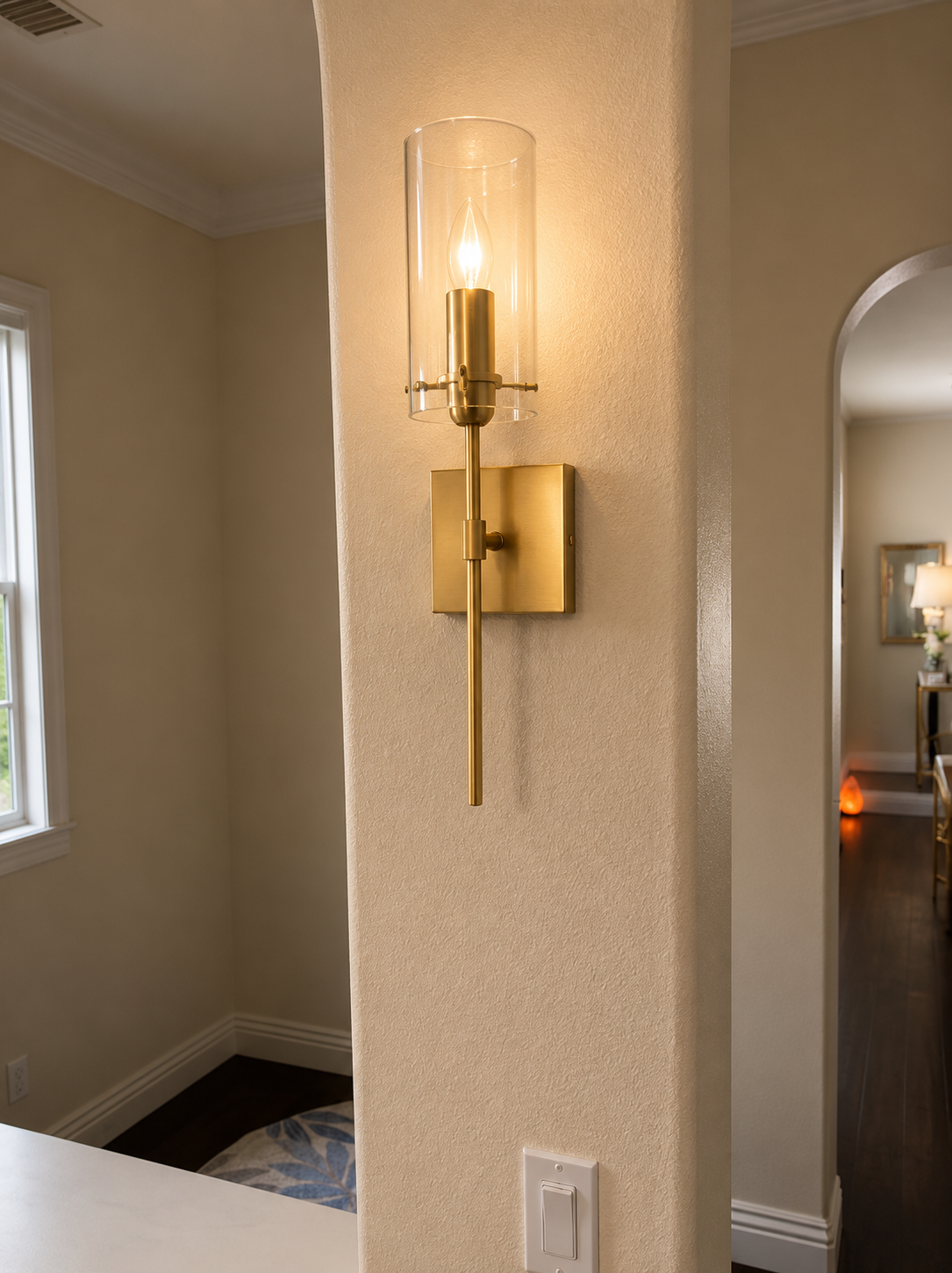 Gold wall sconce with clear glass shade on beige textured wall in a hallway