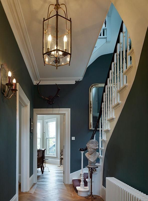 Narrow hallway with dark walls, hanging lanterns, white trim, and a curved staircase beside a bust statue.