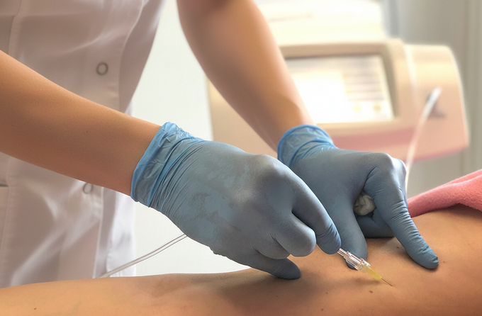 Persona con guanti blu che pratica un'iniezione a una gamba; ambiente medico, attrezzatura sullo sfondo.